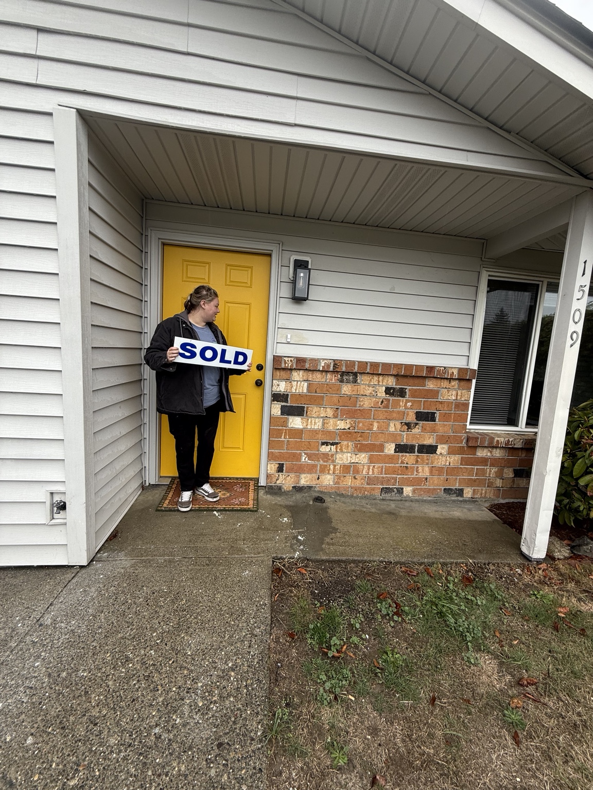 Happy homebuyer with a sold sign at a yellow front door